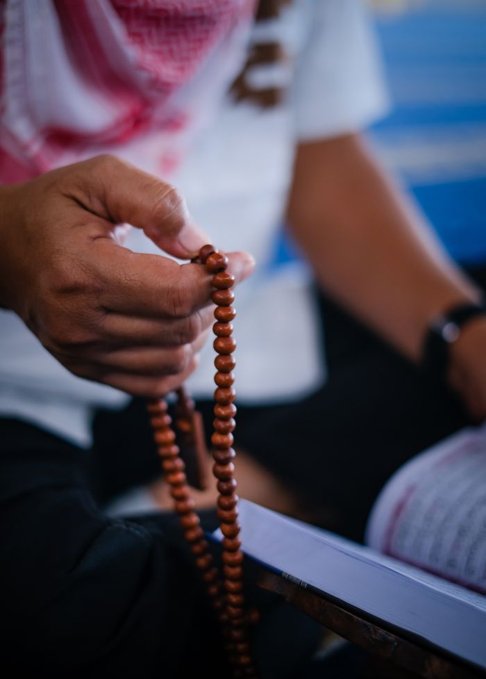 A Muslim man sits in a mosque holding prayer beads, engaged in meditation.
